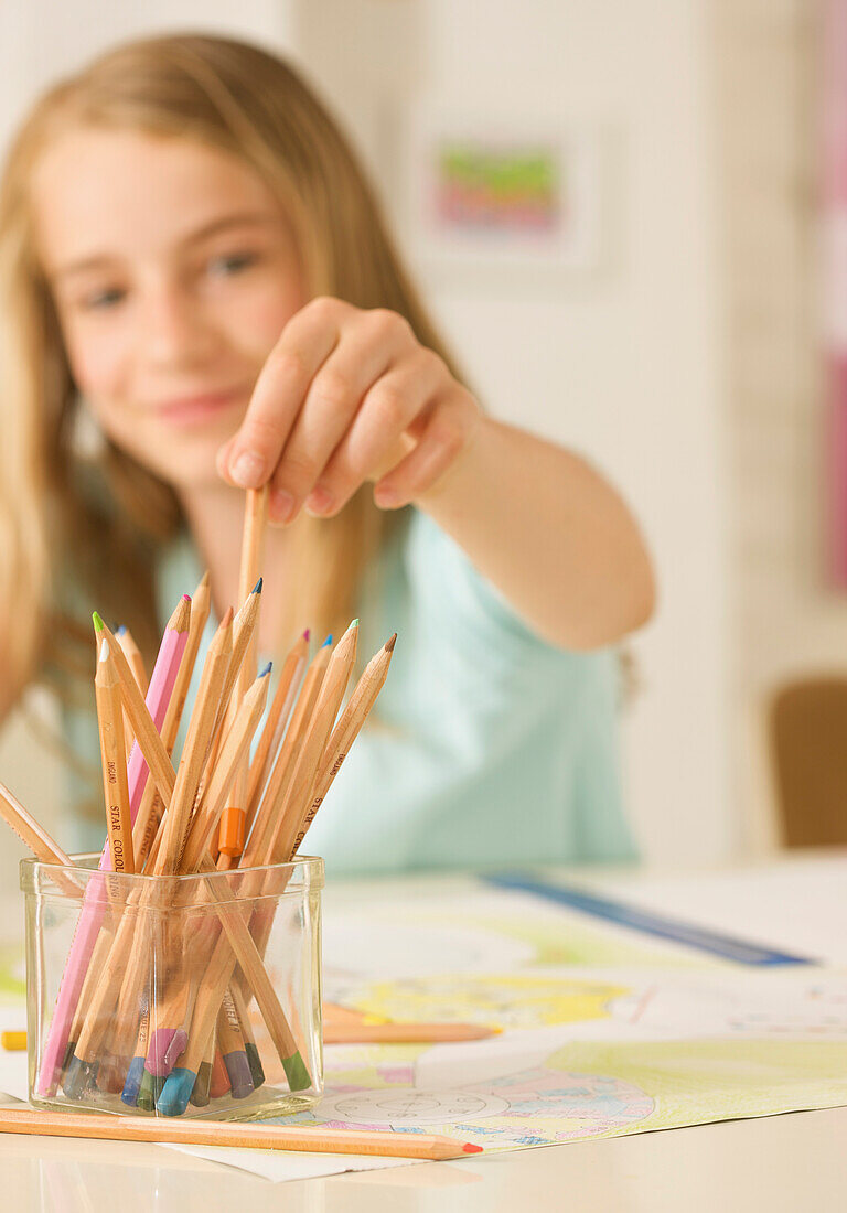 Young girl choosing a  coloring pencil from container\n