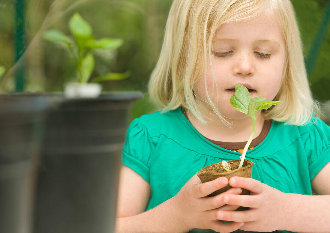 Close up of a young blonde girl inhaling and holding a seedling pot\n