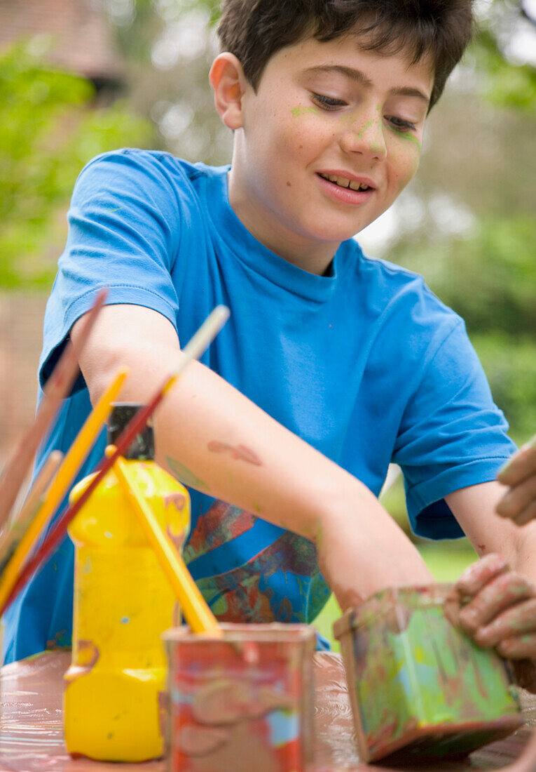 Young boy smiling with one hand in a watercolor paint container\n