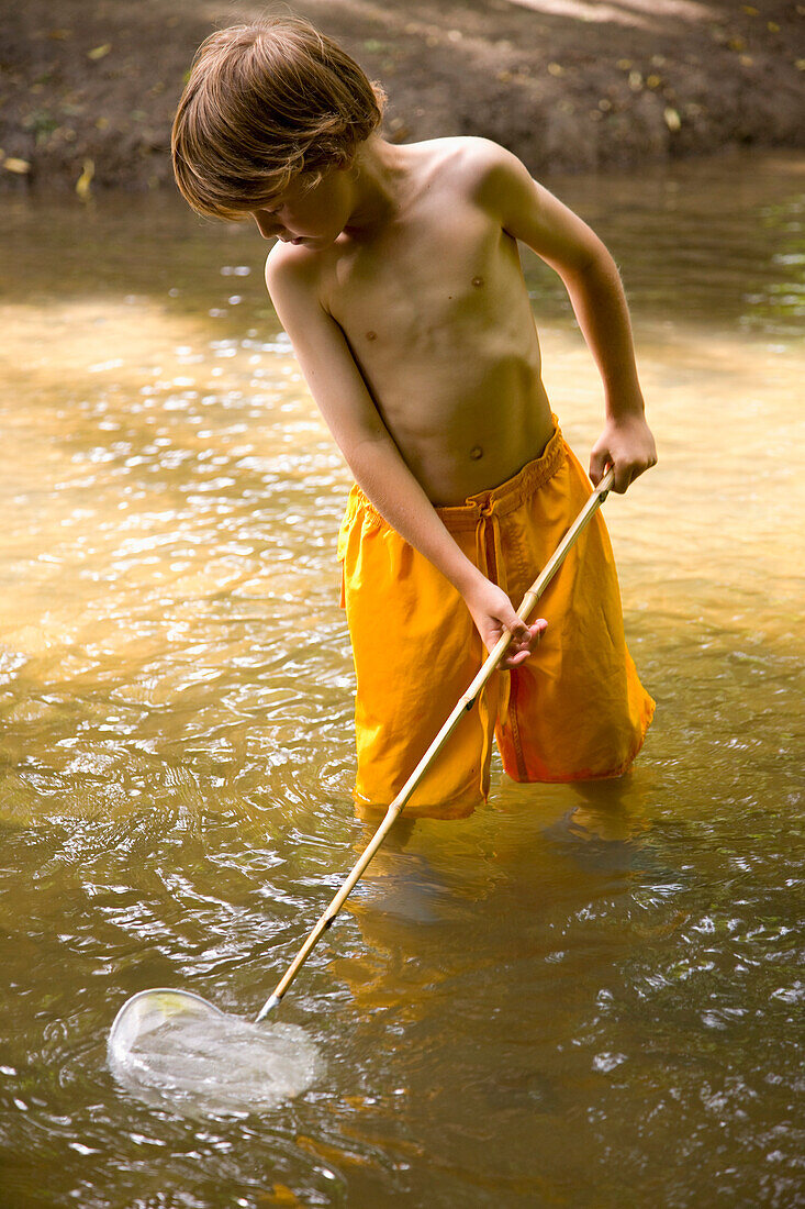 Young boy fishing in a river with fishing net\n