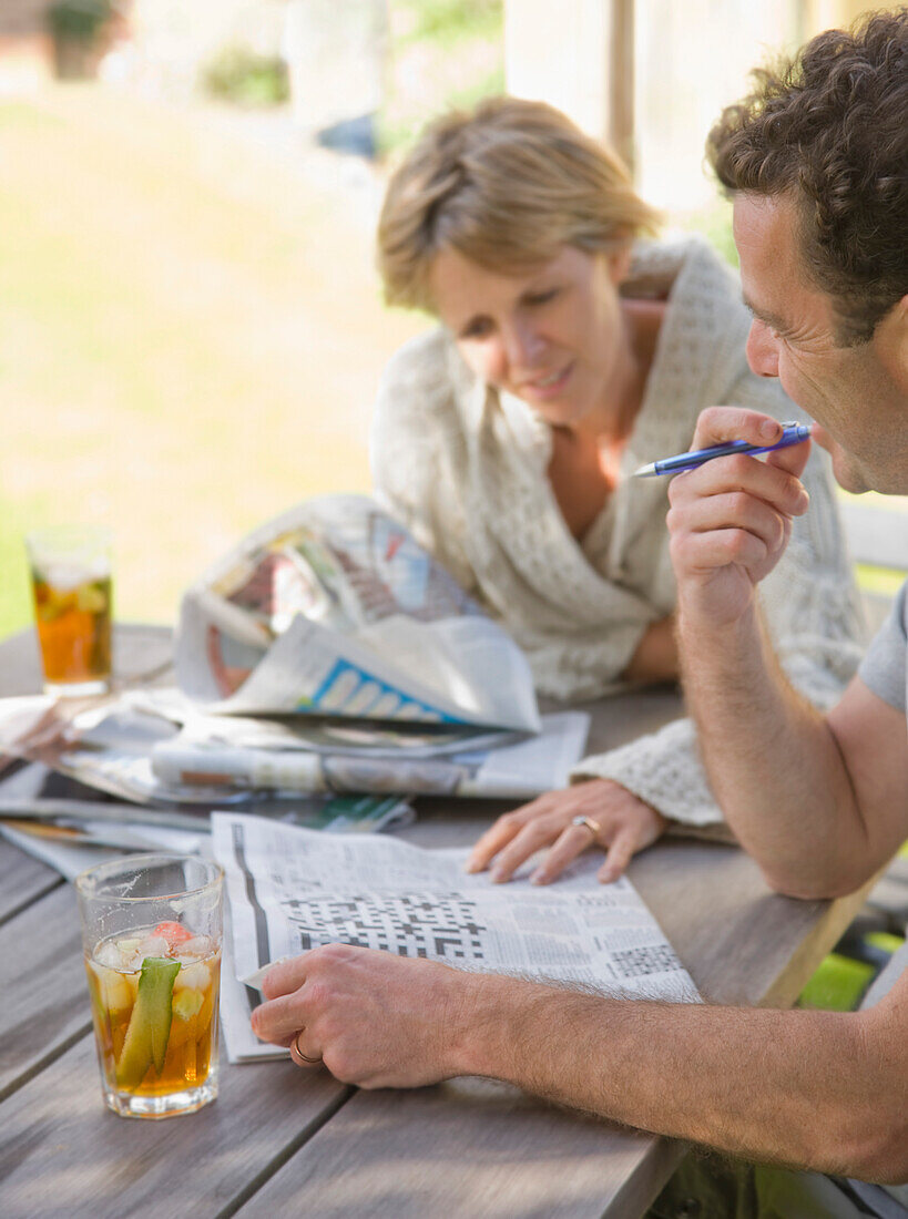 Couple sitting outside drinking cocktails and doing crossword\n