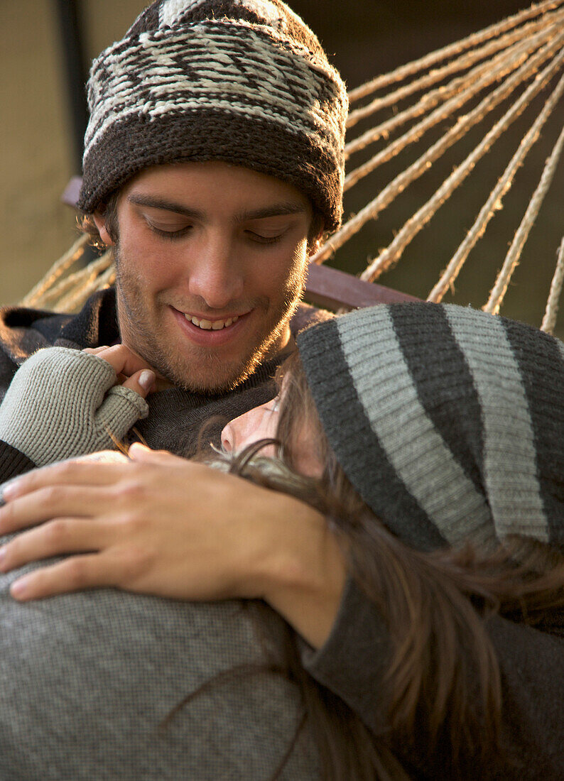 Young couple lying on hammock embracing and looking at each other\n