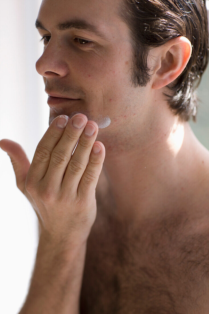 Close up of young man applying moisturizer\n