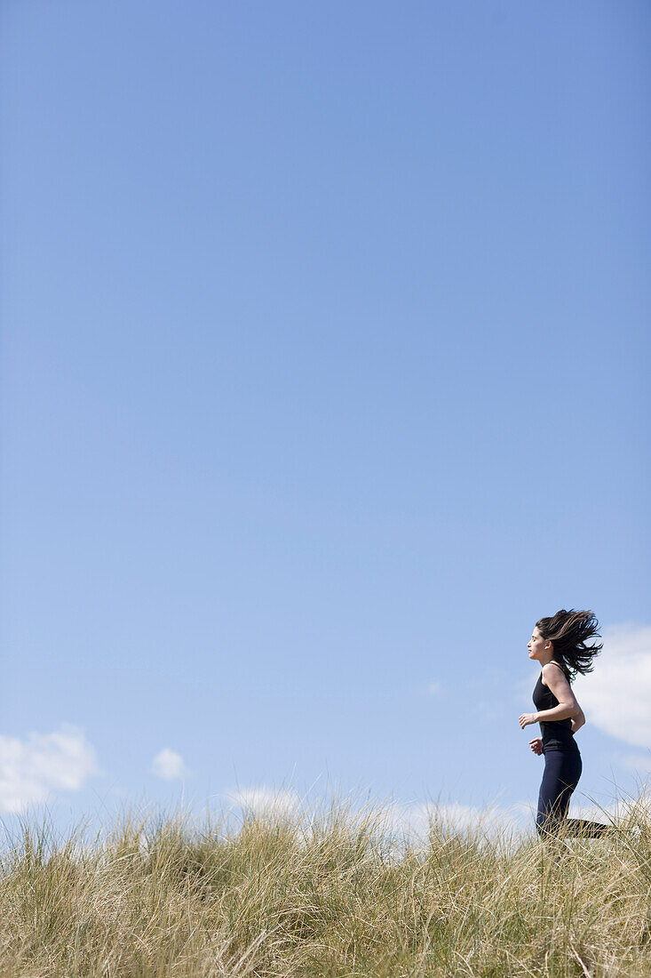 Young woman running through sand dunes\n