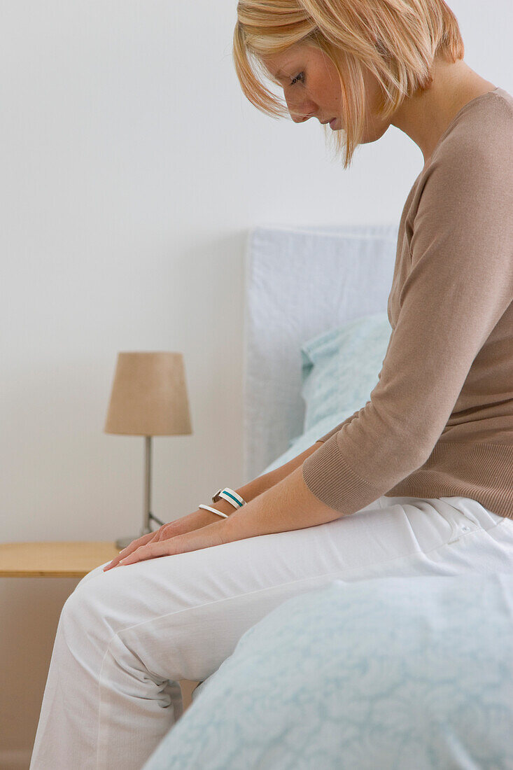 Woman sitting on a bed looking down\n