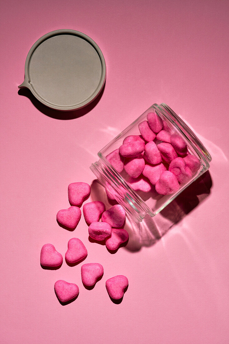 Pink candy hearts spilling from glass jar on pink background\n