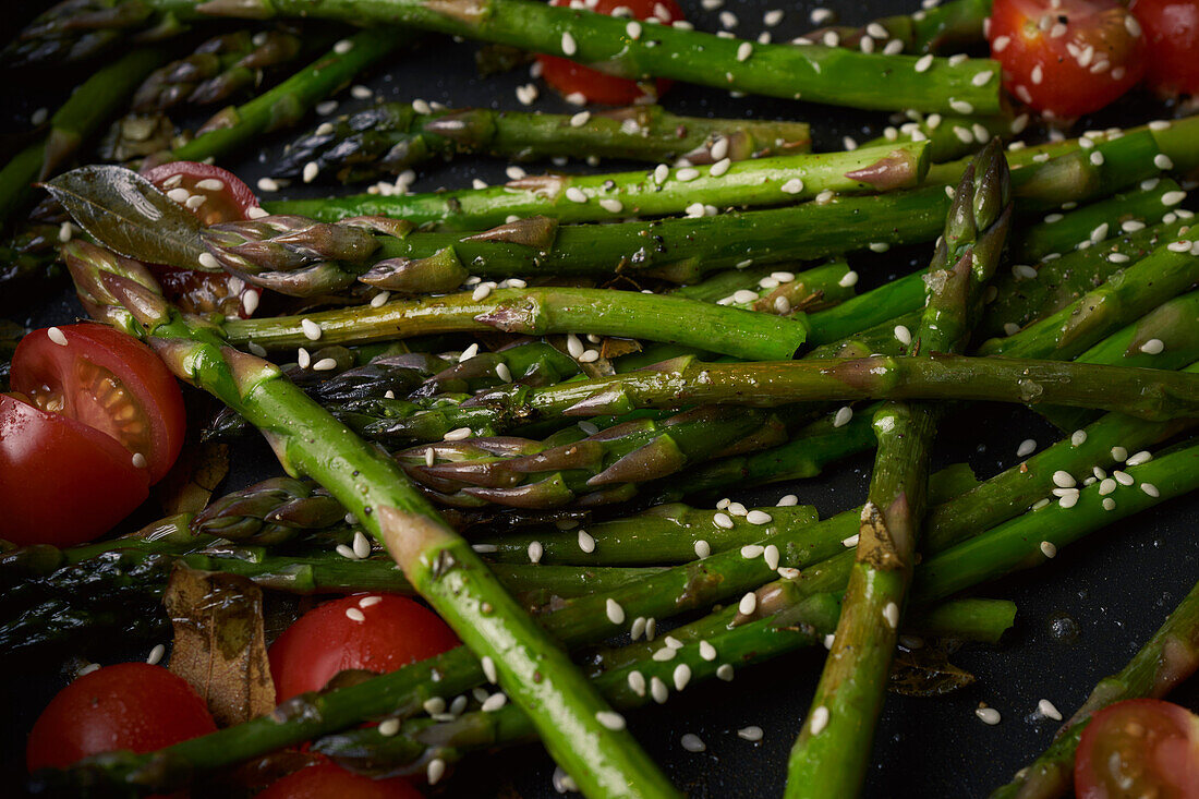Close up asparagus and cherry tomatoes cooking in pan with sesame seeds\n
