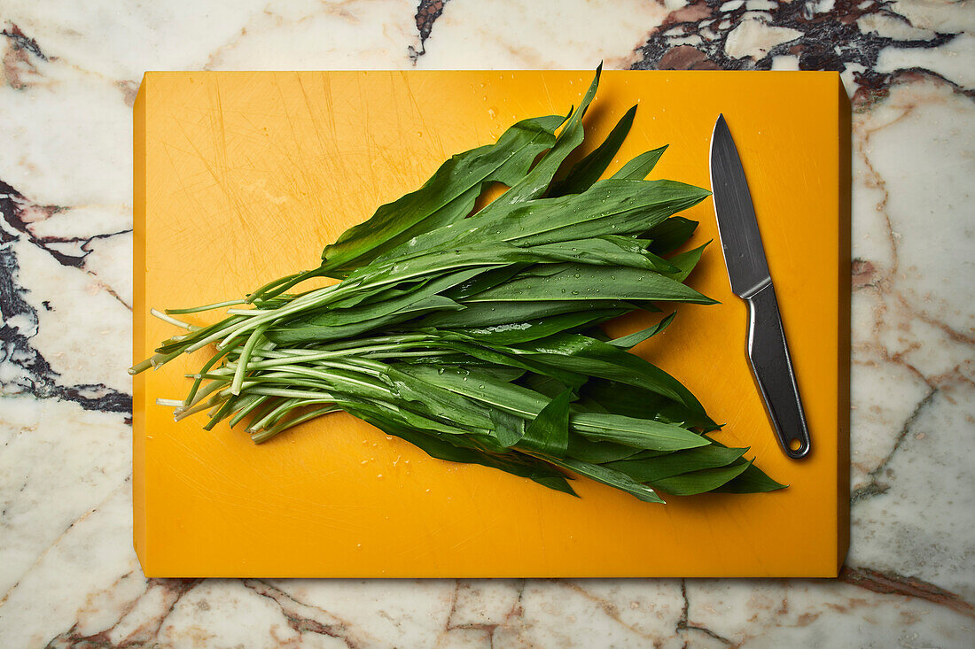 Green wild garlic leaves on cutting board next to knife\n
