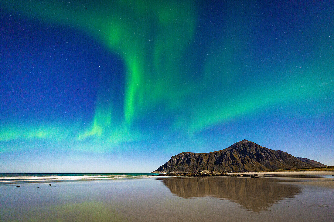 Aurora Borealis (Northern Lights) over mountains reflected on Skagsanden beach washed by waves, Ramberg, Lofoten Islands, Nordland, Norway, Scandinavia, Europe\n