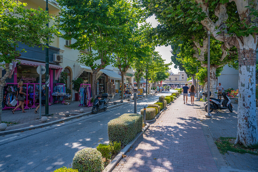 Blick auf Geschäfte in einer von Bäumen gesäumten Straße, Kos-Stadt, Kos, Dodekanes, Griechische Inseln, Griechenland, Europa