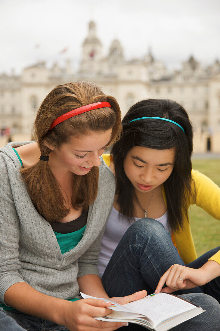 Two teenaged girl reading a book in front of  London Horse Guards Parade\n
