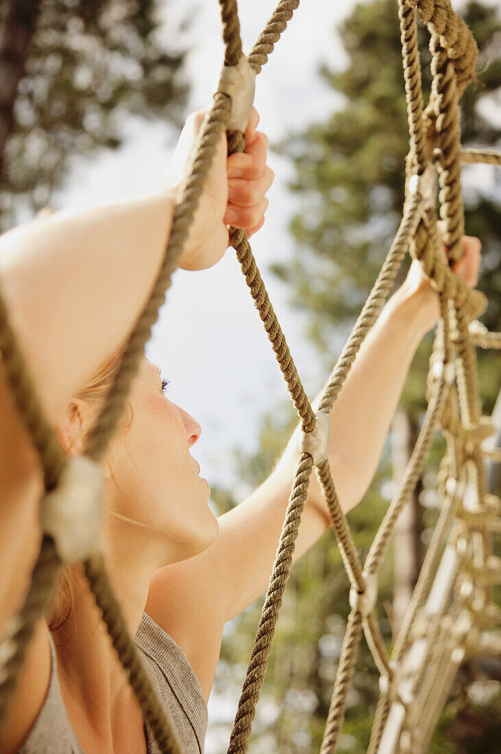 Young woman at obstacle course climbing a cargo net\n
