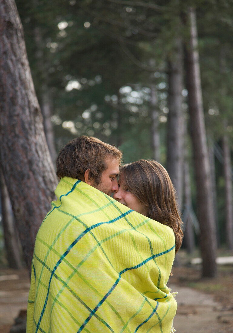 Junges Paar steht in einer Decke eingewickelt im Wald und sieht sich an