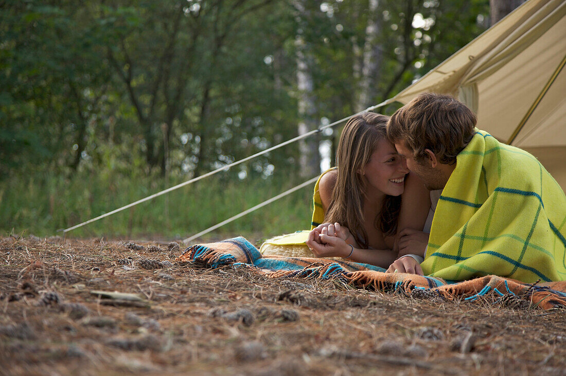 Young couple lying in front of a tent entrance looking at each other\n