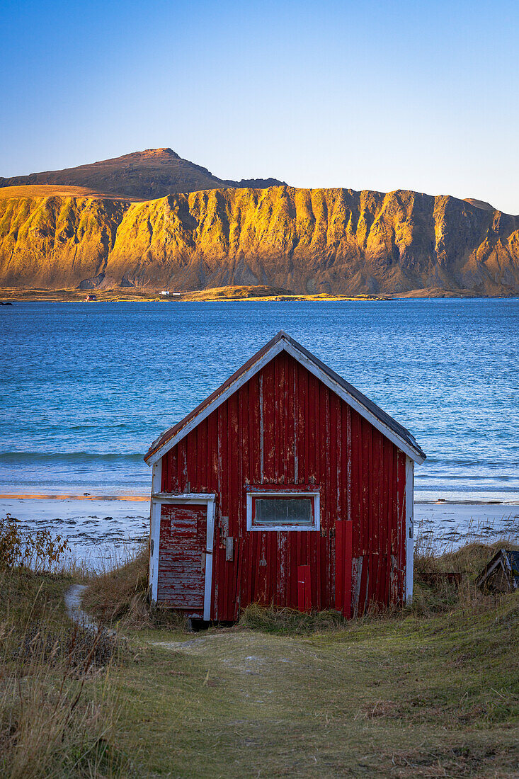 Rote Fischerhütte am Strand von Ramberg mit Bergen im Hintergrund in der Morgendämmerung, Flakstad, Lofoten Inseln, Nordland, Norwegen, Skandinavien, Europa