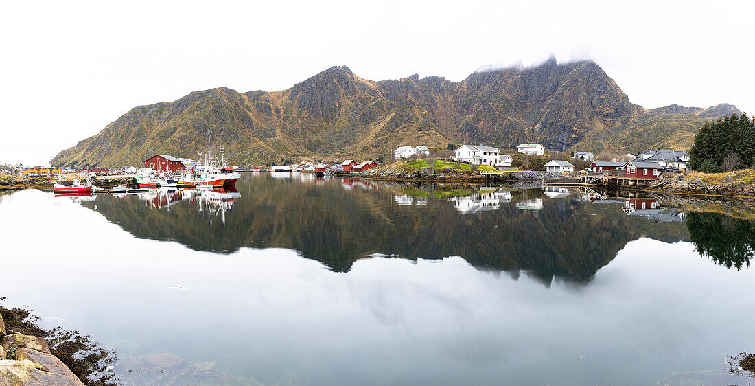 Fishing village of Ballstad and mountains mirrored in the calm waters of a fjord, Vestvagoy, Lofoten Islands, Nordland, Norway, Scandinavia, Europe\n