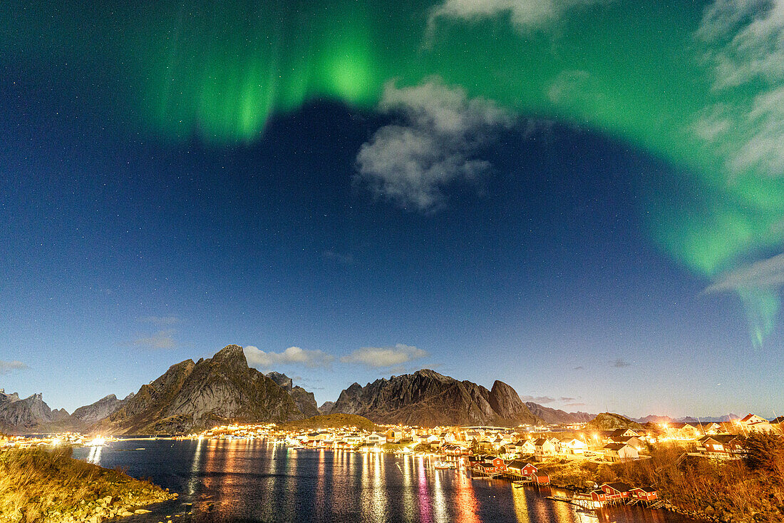 Beleuchteter Hafen von Reine spiegelt sich im kalten arktischen Meer während der Aurora Borealis (Nordlicht), Reine, Lofoten, Nordland, Norwegen, Skandinavien, Europa