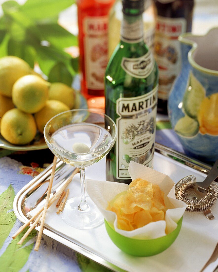 Martini in glass and bottle and potato crisps on tray