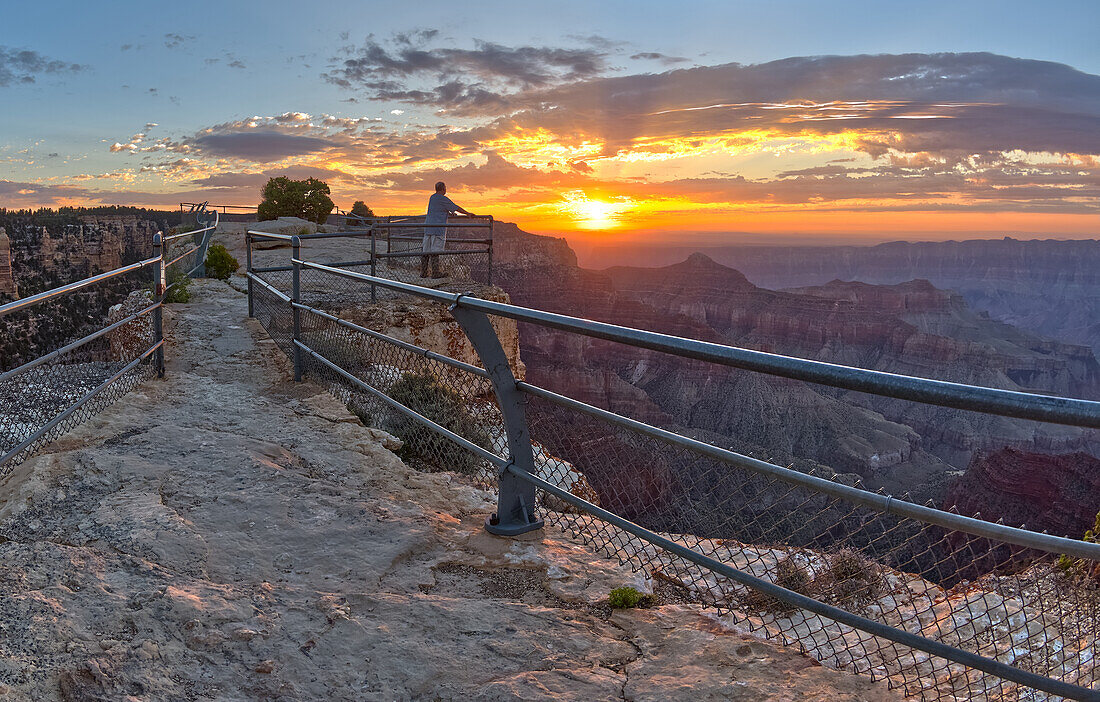 A lone hiker on Angels Window Overlook at Grand Canyon North Rim Arizona looking out at the sunrise.\n