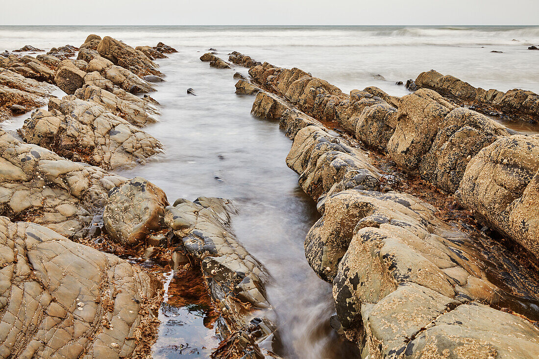 Eine steigende Flut bringt den Atlantik um und über die Felsen am Welcombe Mouth, einer abgelegenen Bucht bei Hartland, an der Atlantikküste von Devon, England, Vereinigtes Königreich, Europa