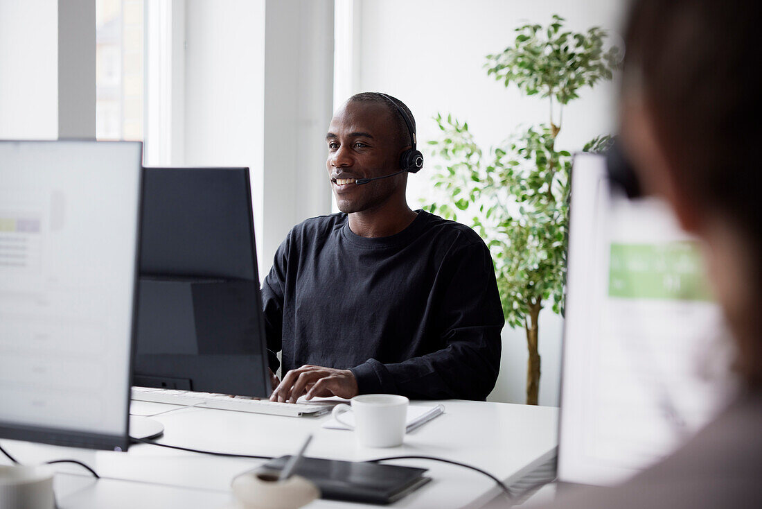 Smiling mature businessman using headset and desktop PC  in office\n