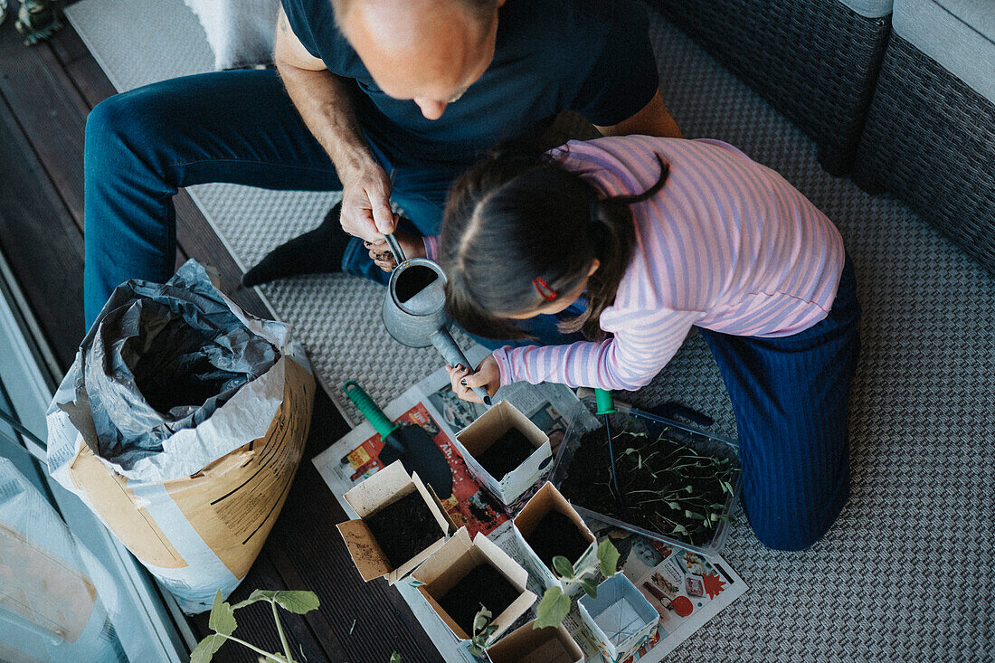 Father and daughter bonding over planting seedlings on balcony\n