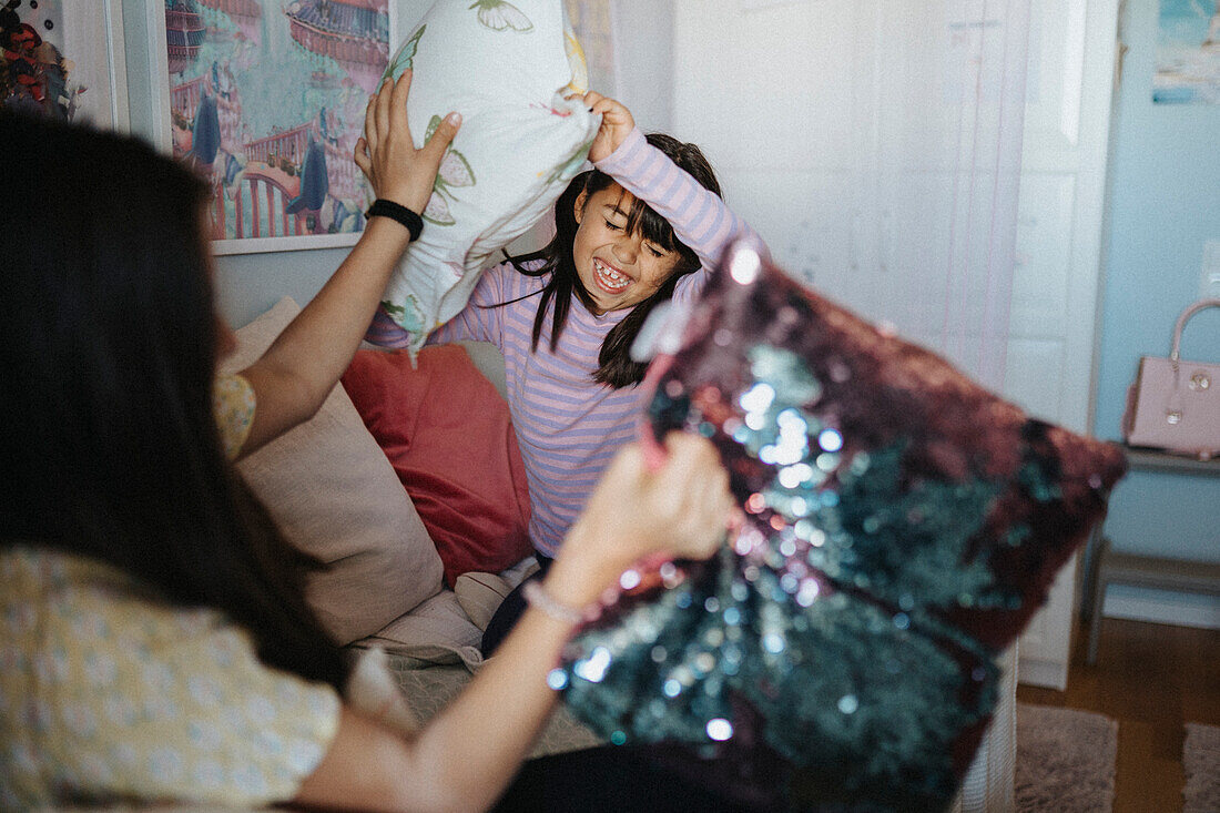 Happy sisters having pillow fight at home\n