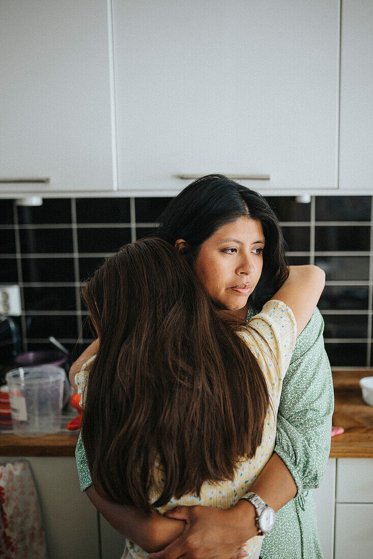 Loving mother hugging daughter at home\n