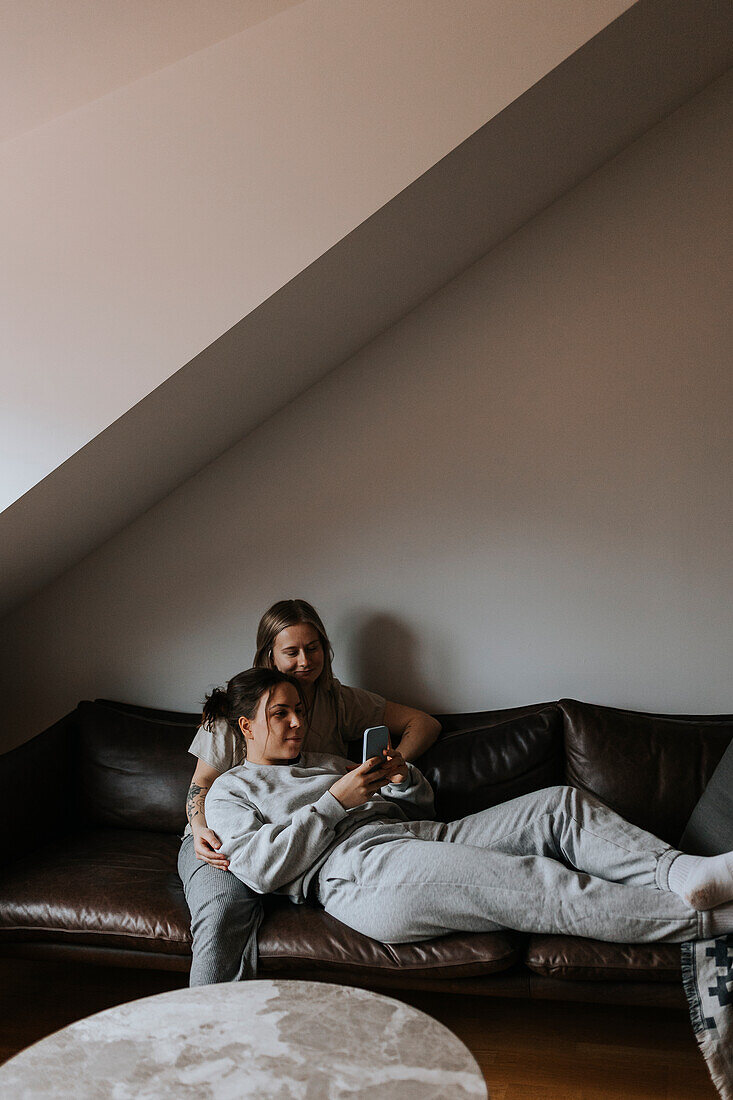 Female couple relaxing together on sofa and looking at cell phone\n