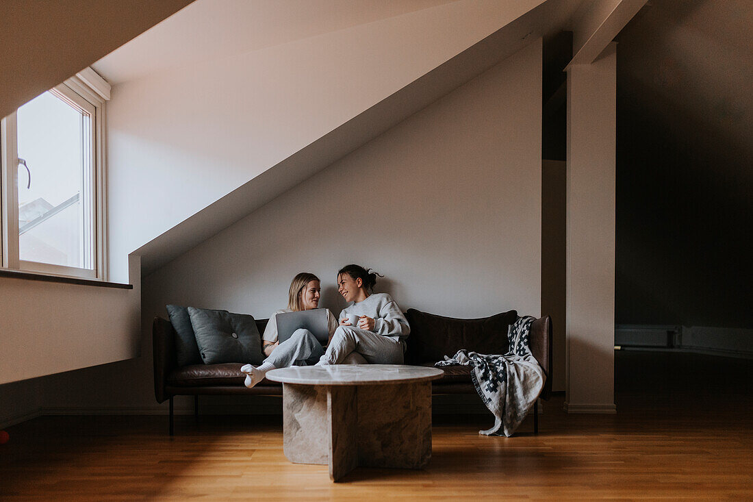 Female couple sitting together on sofa and smiling\n