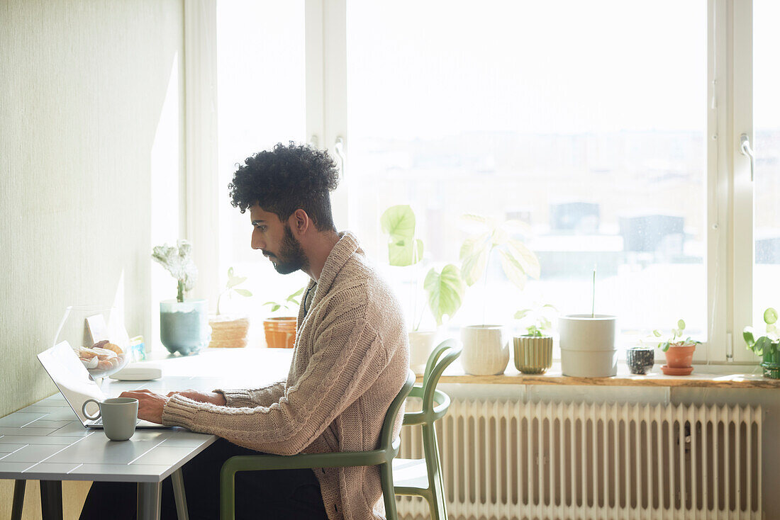 Man using laptop at table while drinking coffee\n