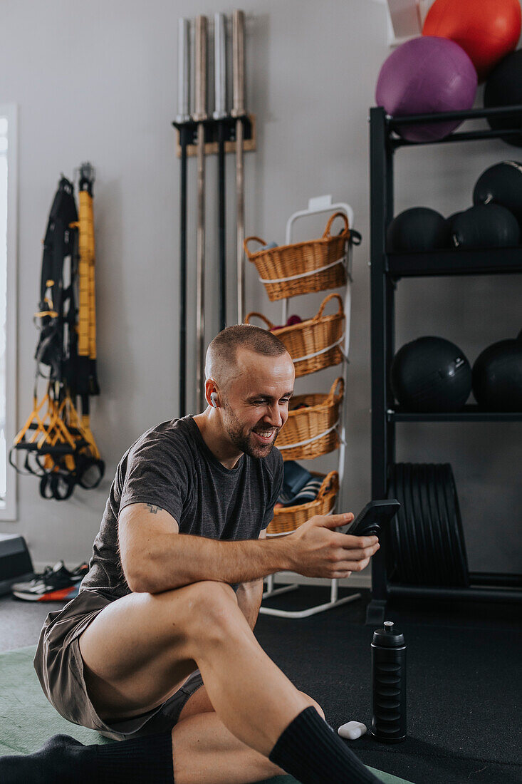 Man using phone while stretching in gym\n