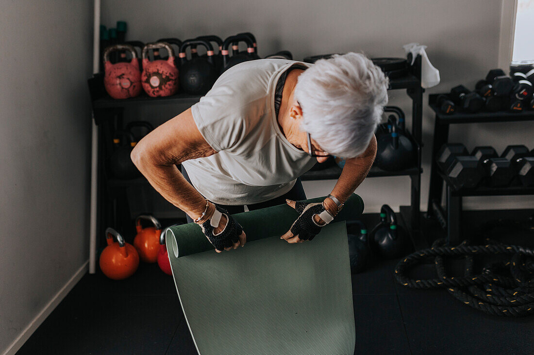 Senior woman rolling up mats after workout at gym\n