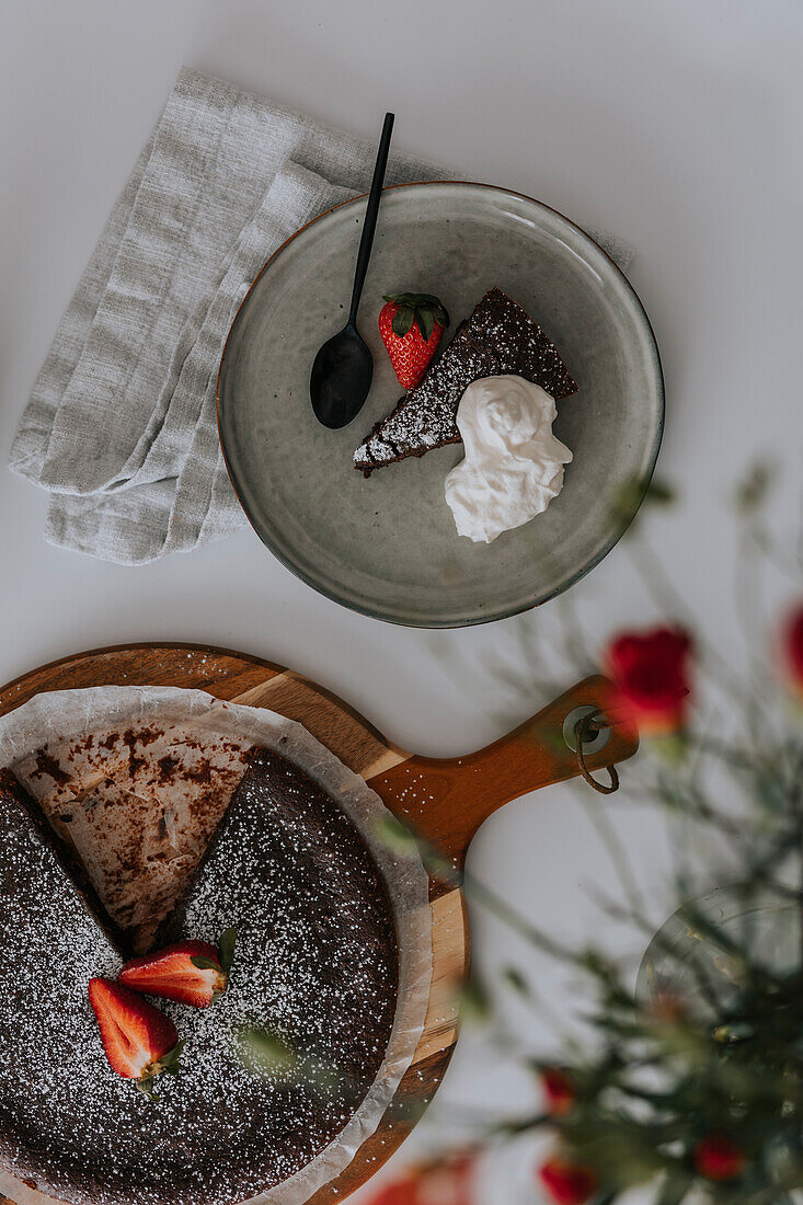 Freshly baked chocolate cake with strawberries and cream on table\n