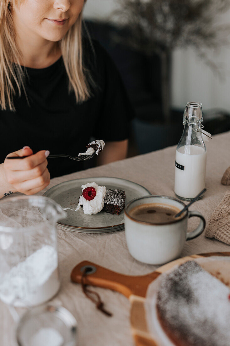 Woman eating chocolate cake with cream and raspberries\n