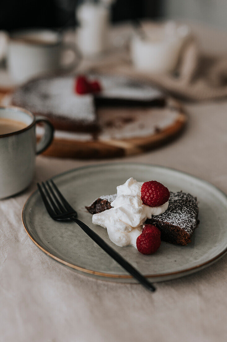 Serving of chocolate cake with cream and raspberries on plate\n