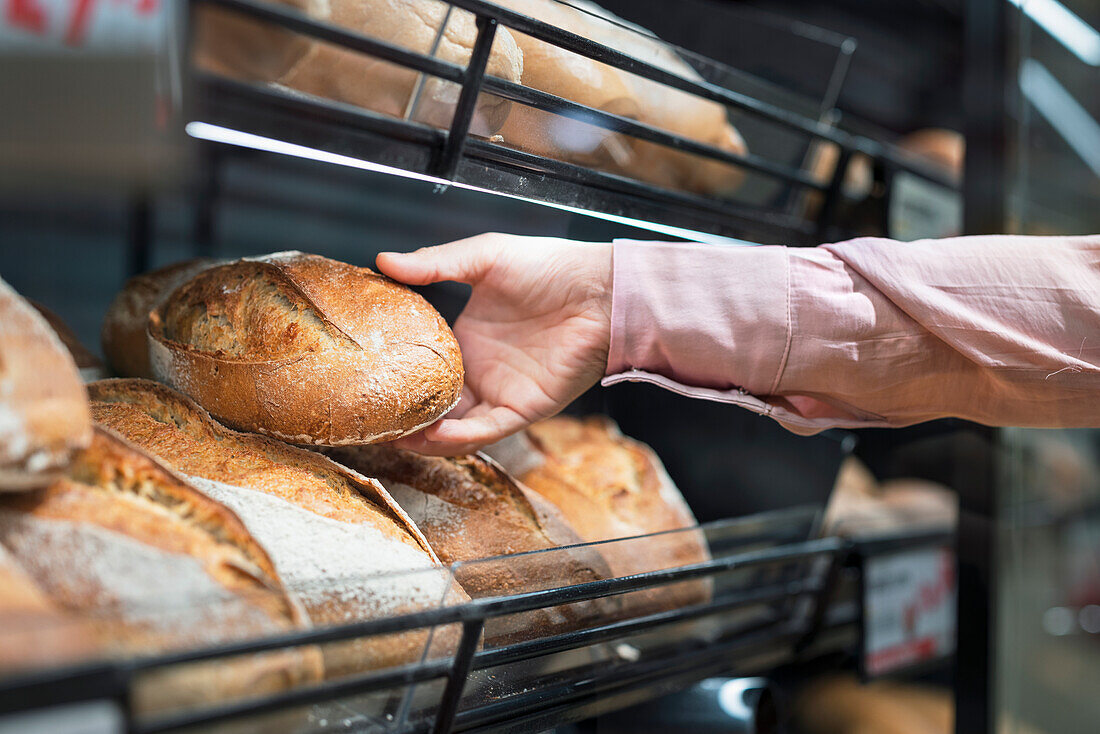 Close-up of man picking bread in bakery section of supermarket\n