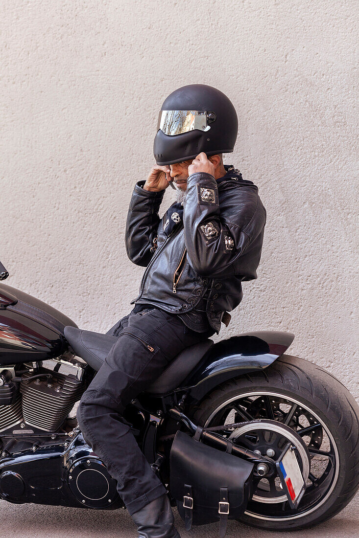 Mature biker in leather clothes putting on helmet\n