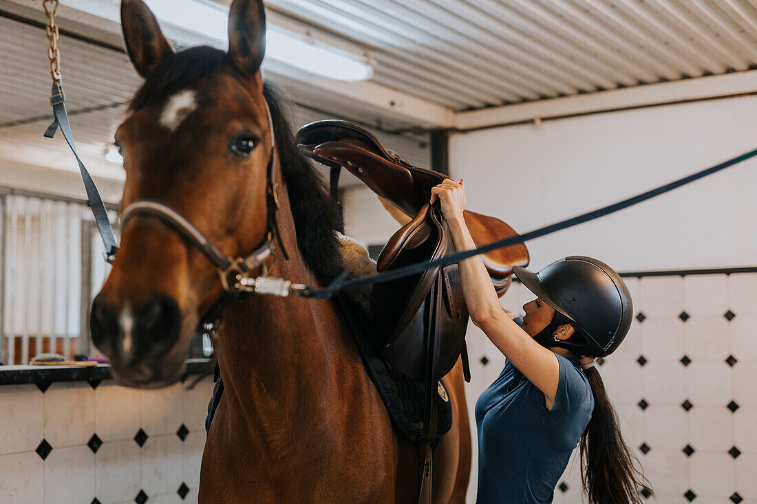 Frau im Stall legt Pferd den Sattel auf