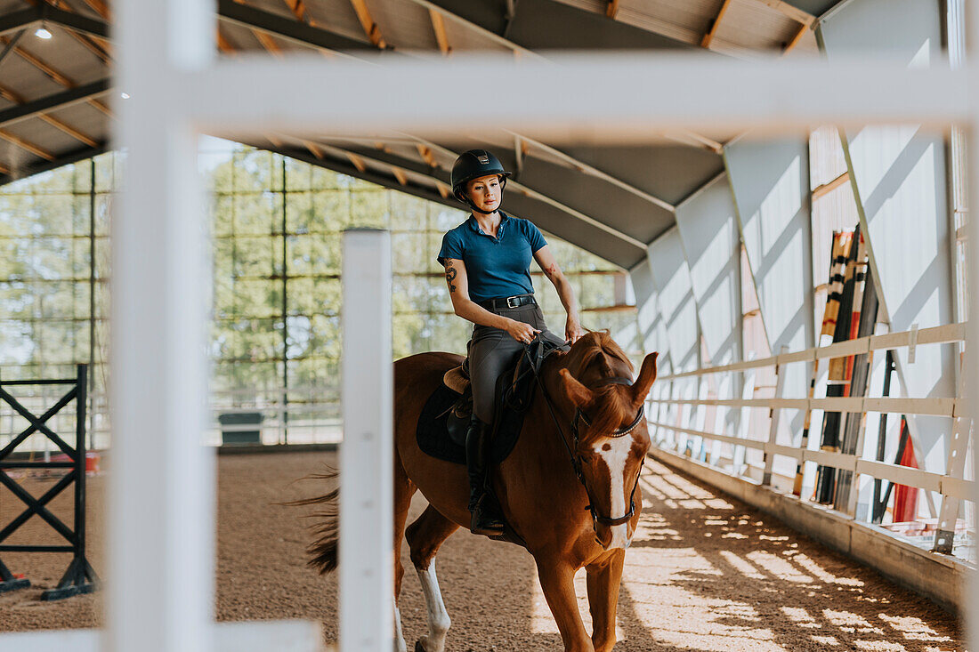 View of female horse rider using indoor riding paddock\n