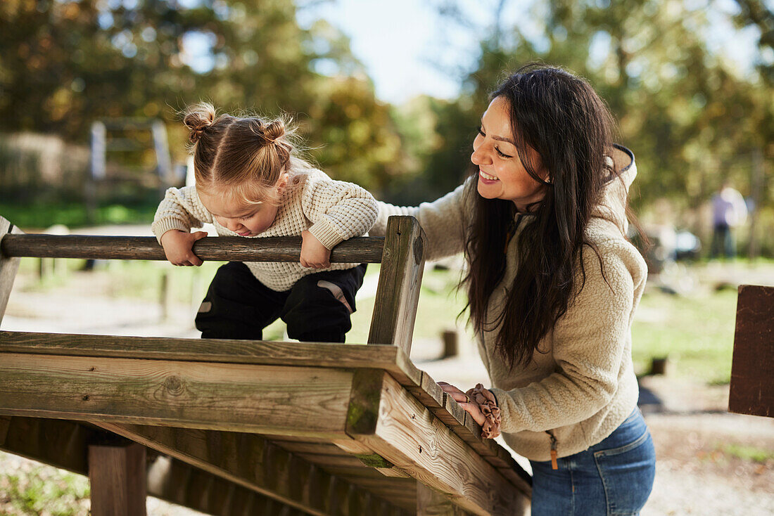 Mutter schaut Tochter beim Spielen auf dem Spielplatz zu