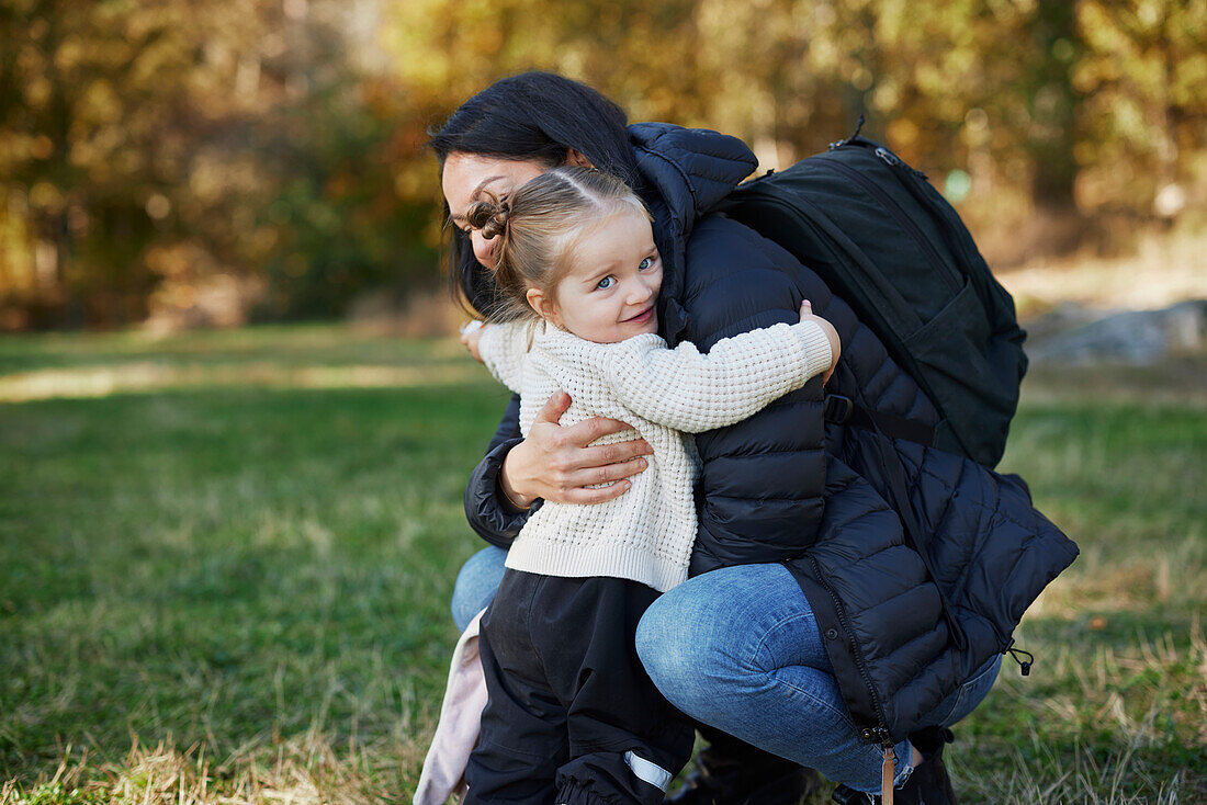 Girl smiling and hugging mother in park\n