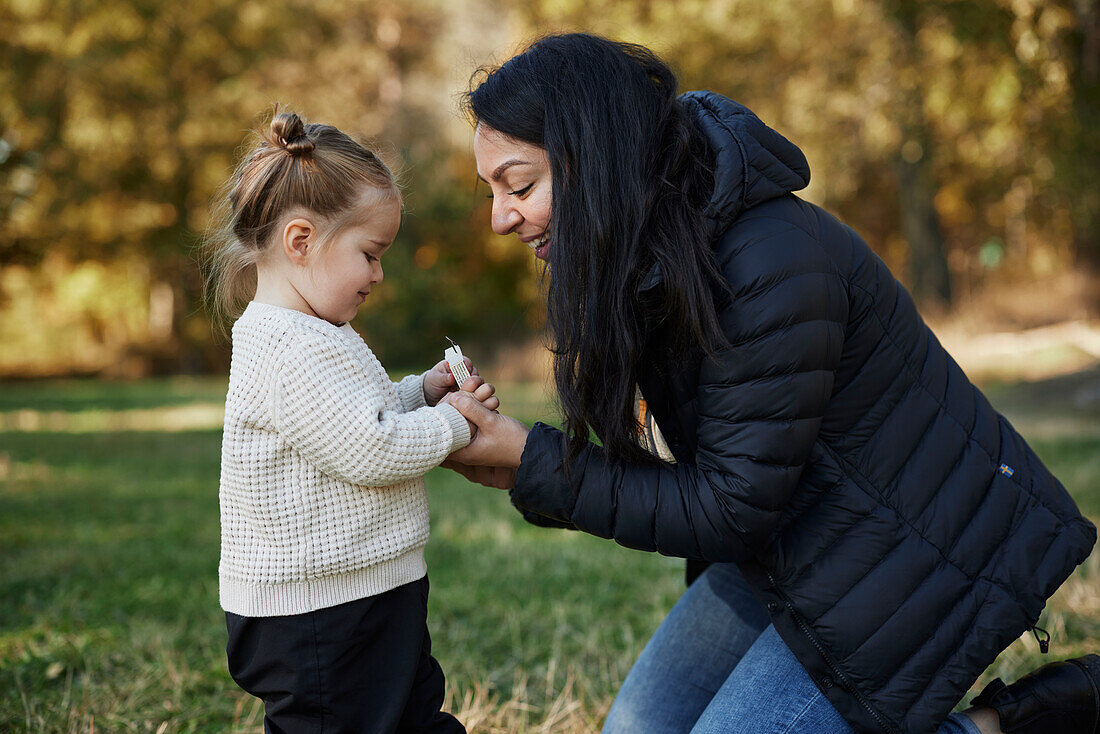 Smiling mother standing with daughter in park\n