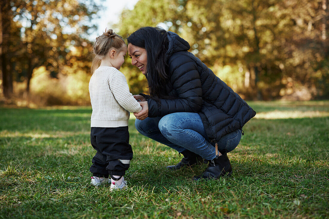 Mother and daughter standing together in autumn park\n