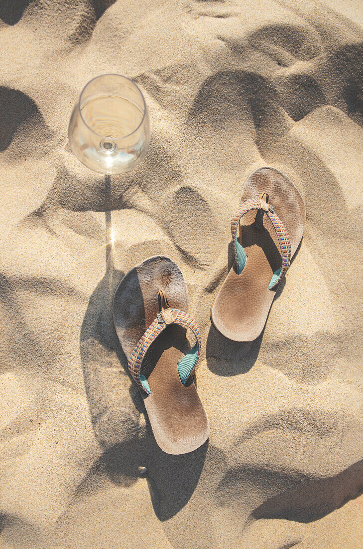 Weinglas und Badelatschen am Sandstrand