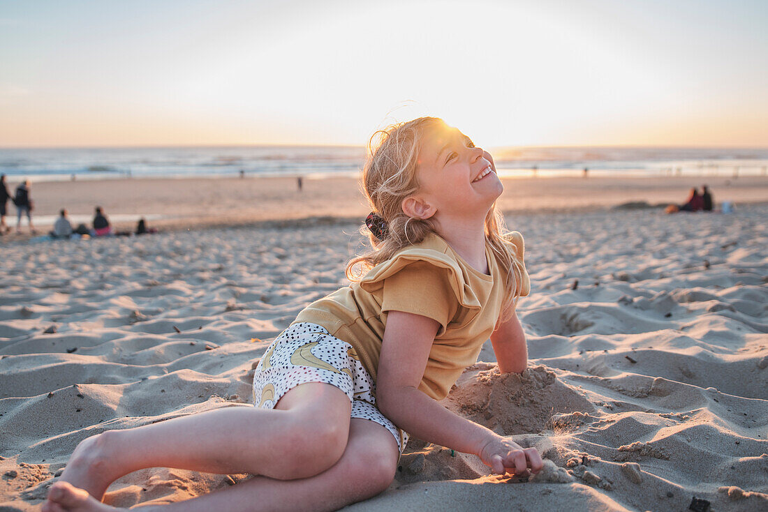 Blondes Mädchen spielt bei Sonnenuntergang am Strand