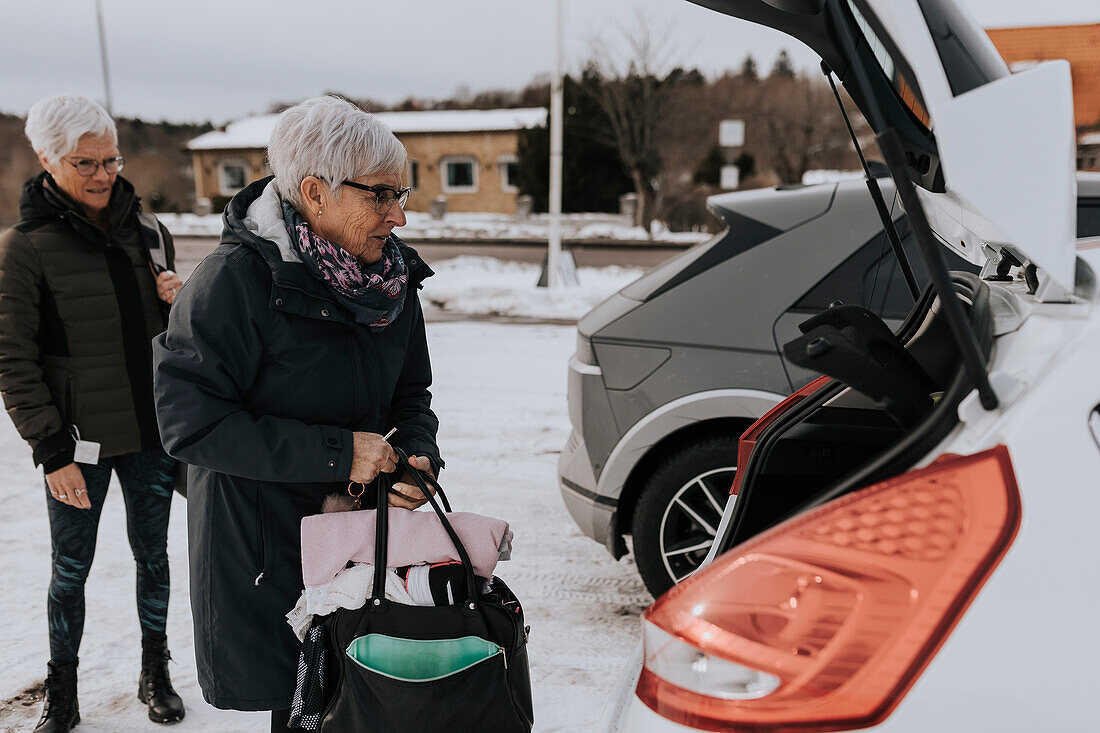 Senior women packing bags in car after workout in gym\n