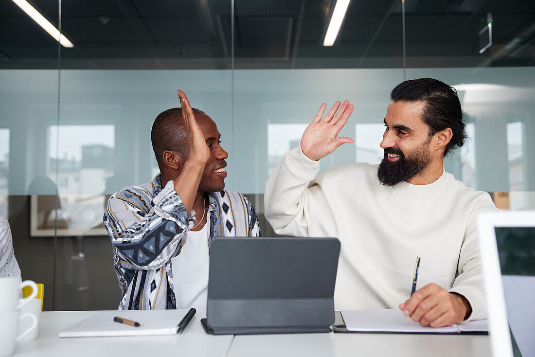 Smiling coworkers sitting at business meeting and giving each other high five\n