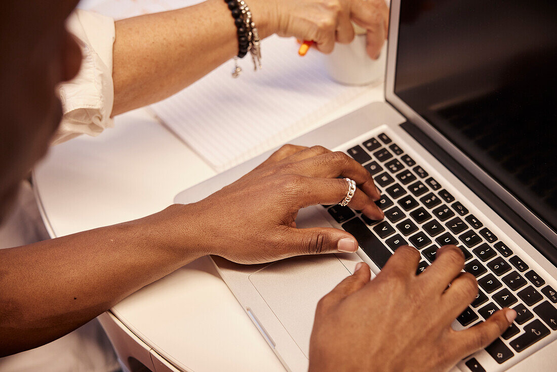Blick von oben auf die Hände einer Frau bei der Arbeit mit einem Laptop