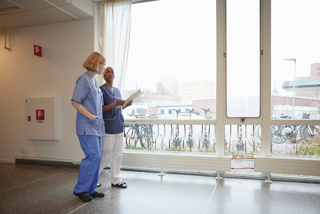 Female doctors standing at hospital corridor and talking to each other\n